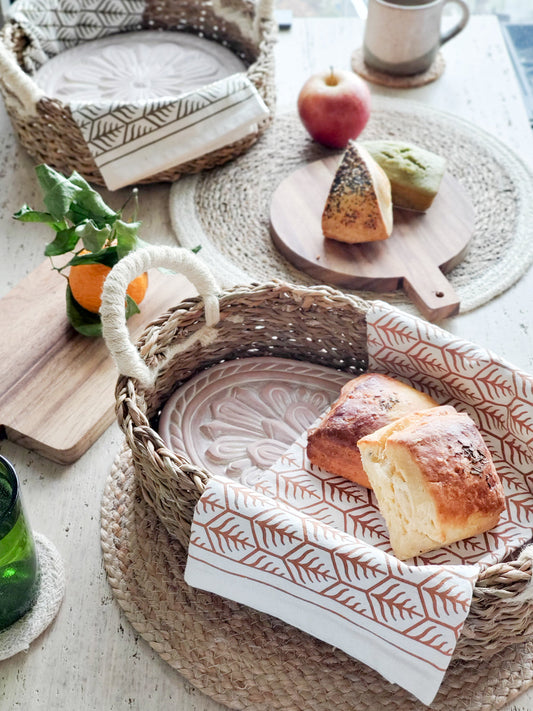 The Gathering Bread Basket with warm bread, linen napkin, and terracotta warming stone on a table.